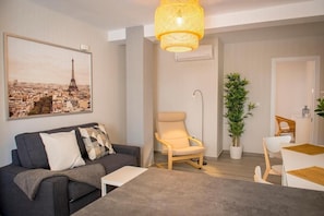 Una sala moderna con un sofá, un sillón, una mesa de comedor y una gran fotografía enmarcada de un paisaje urbano.