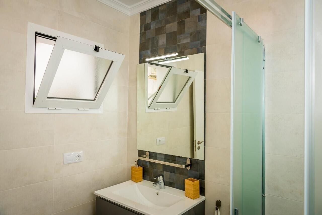 Un baño con lavamanos blanco, un espejo y una puerta de ducha.