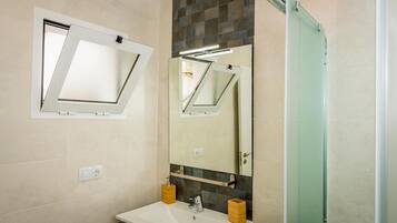 Un baño con lavamanos blanco, un espejo y una puerta de ducha.