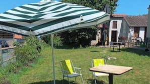 Un espacio al aire libre con césped, una sombrilla a rayas, dos sillas amarillas y una mesa de madera.
