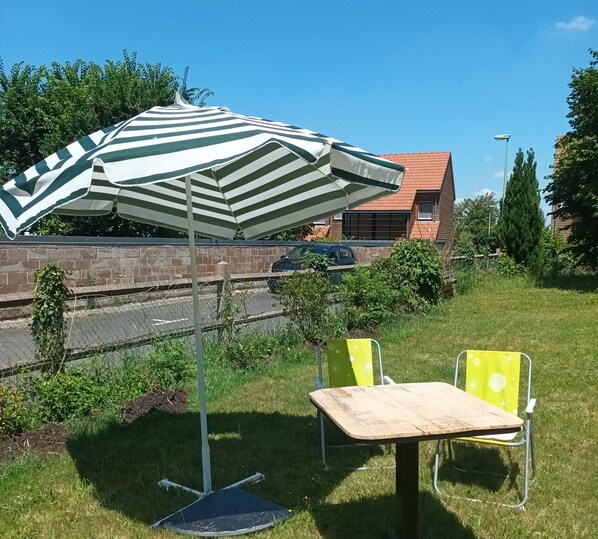 A grassy outdoor area with a striped umbrella, two yellow chairs, and a table.