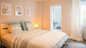 Une chambre à coucher avec un lit, des tables de chevet, une lampe et des œuvres d’art encadrées accrochées au mur.