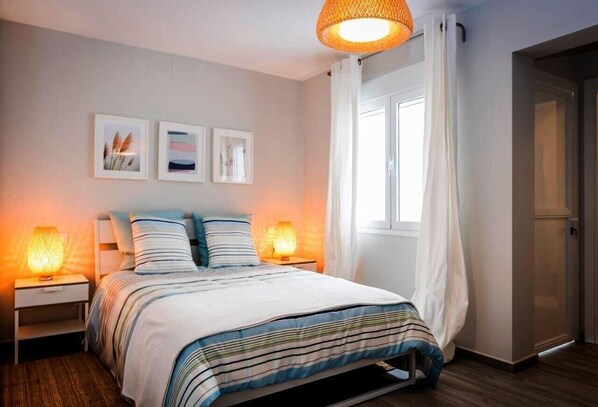 A bedroom with a bed, two bedside lamps, a window with curtains, and wall art.