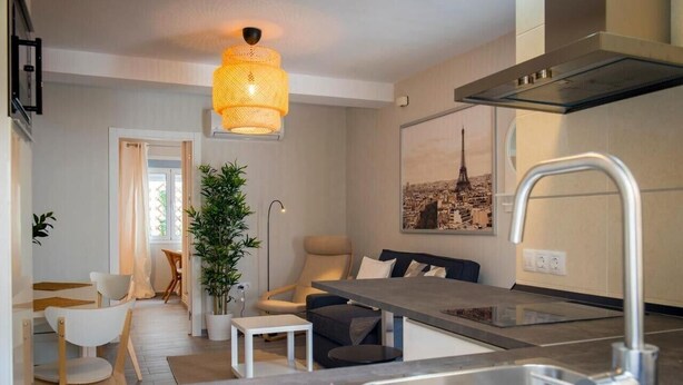 Une cuisine moderne avec un coin repas, un luminaire suspendu et un tableau représentant un paysage urbain accroché au mur.