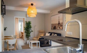 A modern kitchen with a dining area, a hanging light fixture, and a cityscape painting on the wall.