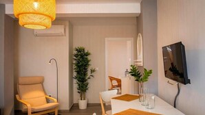 Un salon moderne comprenant un canapé, une table à manger, des chaises, une plante en pot, un téléviseur et un luminaire suspendu.