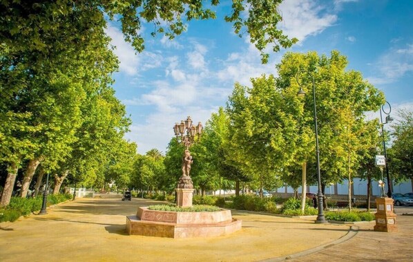 A park with a central statue, trees, and a paved walkway.