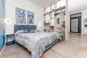 Un dormitorio moderno con cama, mesitas de noche, obras de arte y una pequeña cocina.
