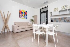 Un salon moderne comprenant un canapé, une table à manger avec des chaises, une machine à café et un coin cuisine avec des étagères.
