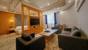 A modern hotel room with a living area, a flat-screen TV, a sofa, a coffee table, and a bed.