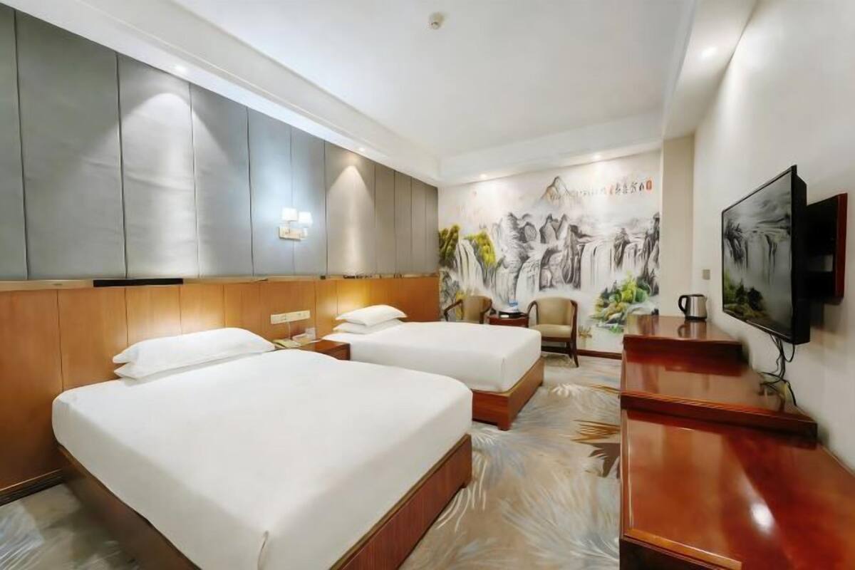 Habitación de hotel con dos camas, un escritorio, una silla, un televisor y una pared decorada con obras de arte.