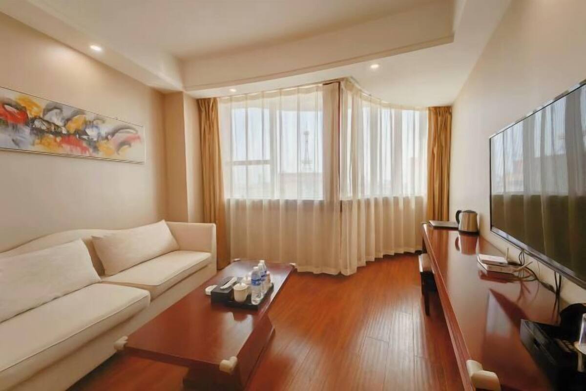 Una habitación de hotel moderna con sofá, mesa de centro, televisor y un amplio ventanal con cortinas.