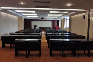 A conference room with rows of tables and chairs, a projector screen, and a podium.