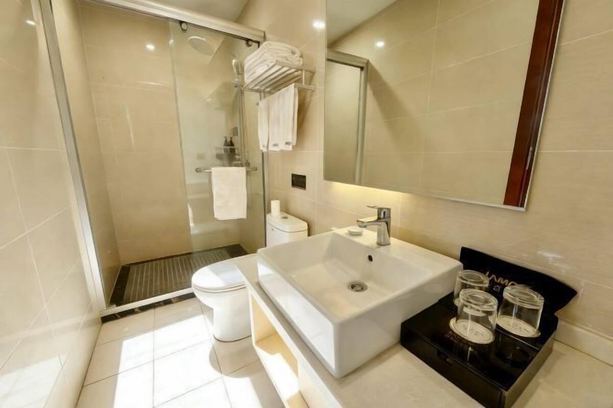 Un baño moderno con ducha envuelta en vidrio, un lavamanos blanco y un jabonera negra.