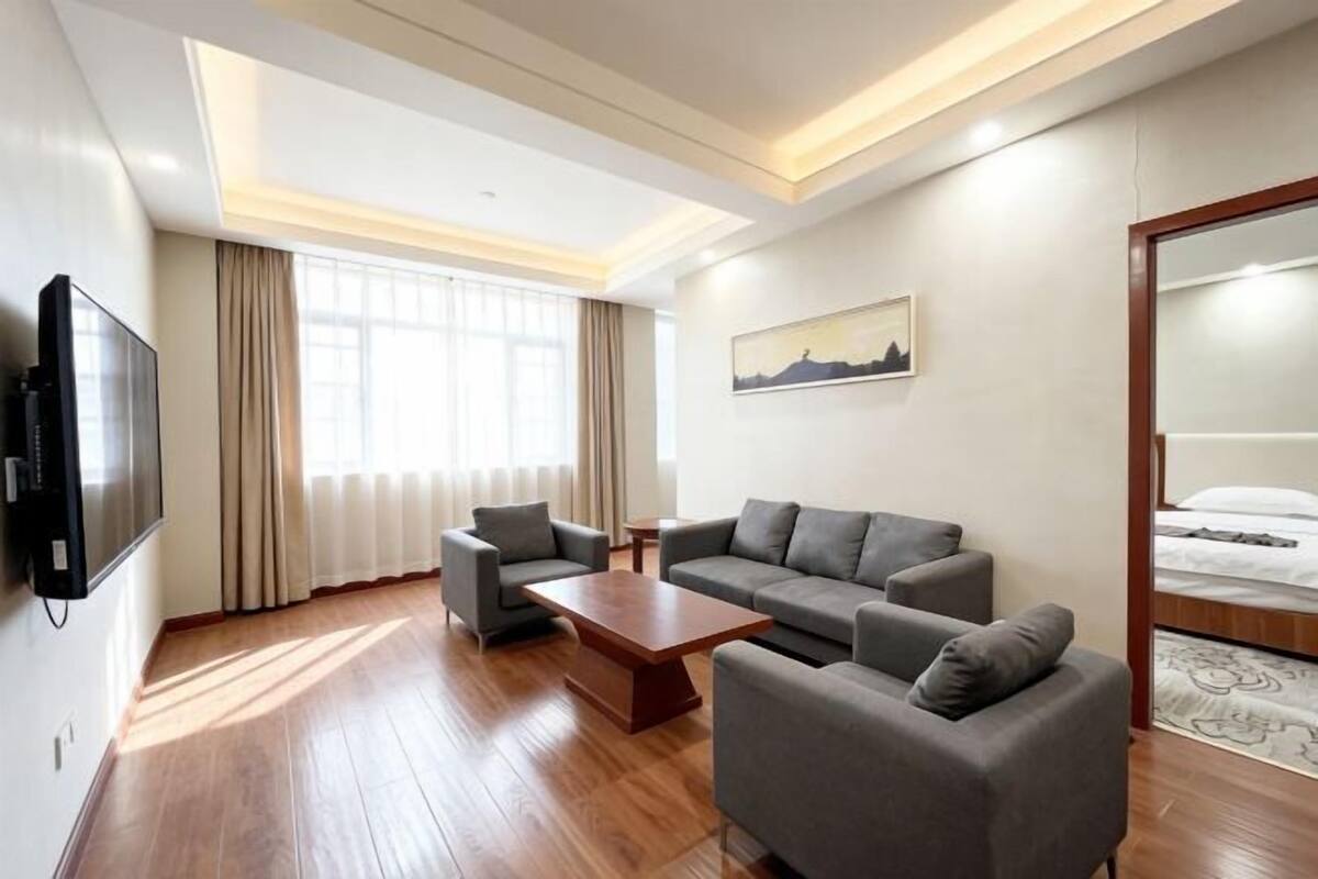 Una habitación de hotel moderna con un conjunto de sofá, una mesa de centro, un televisor de pantalla plana y una cama con cubrecama estampado.