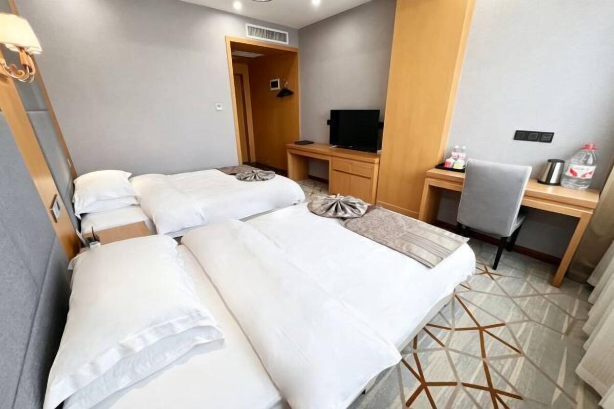 Habitación de hotel con dos camas, un escritorio, una silla, un televisor y una mesita con una botella.