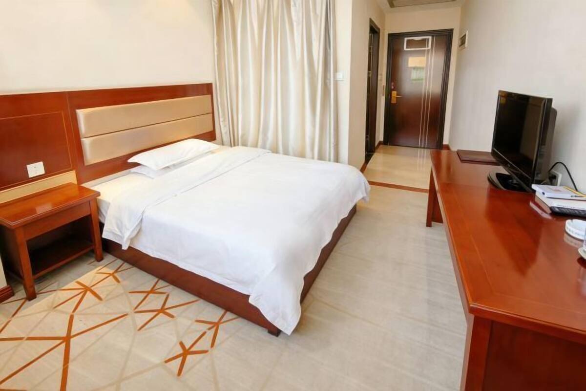 Habitación de hotel con cama, televisión, escritorio y puerta al baño.