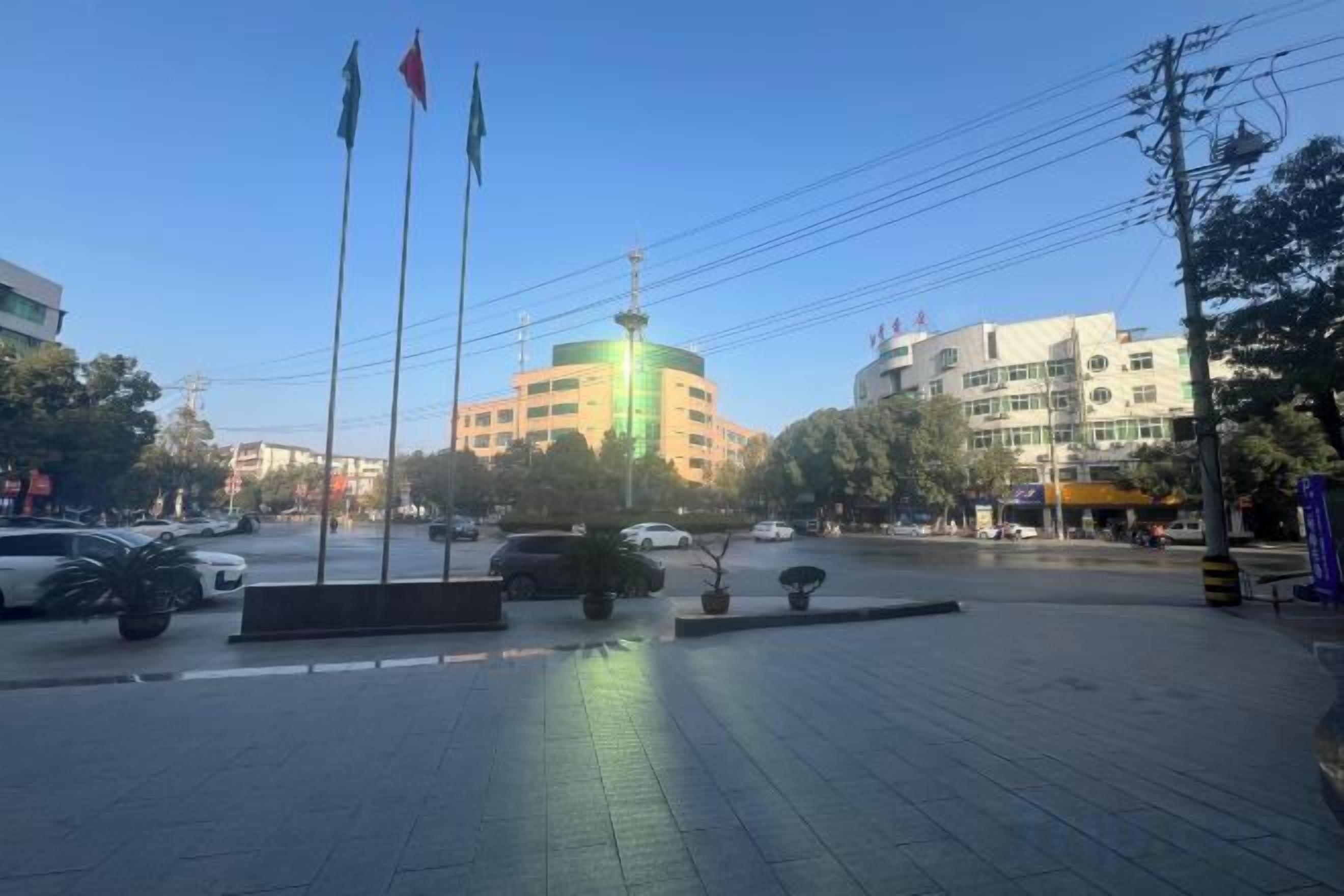 Une place pavée avec une fontaine, des drapeaux et des bâtiments en arrière-plan.