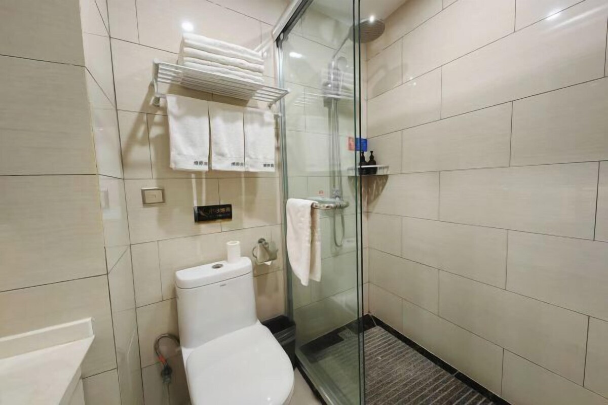 A bathroom with a glass shower enclosure, a toilet, a towel rack, and a soap dispenser.