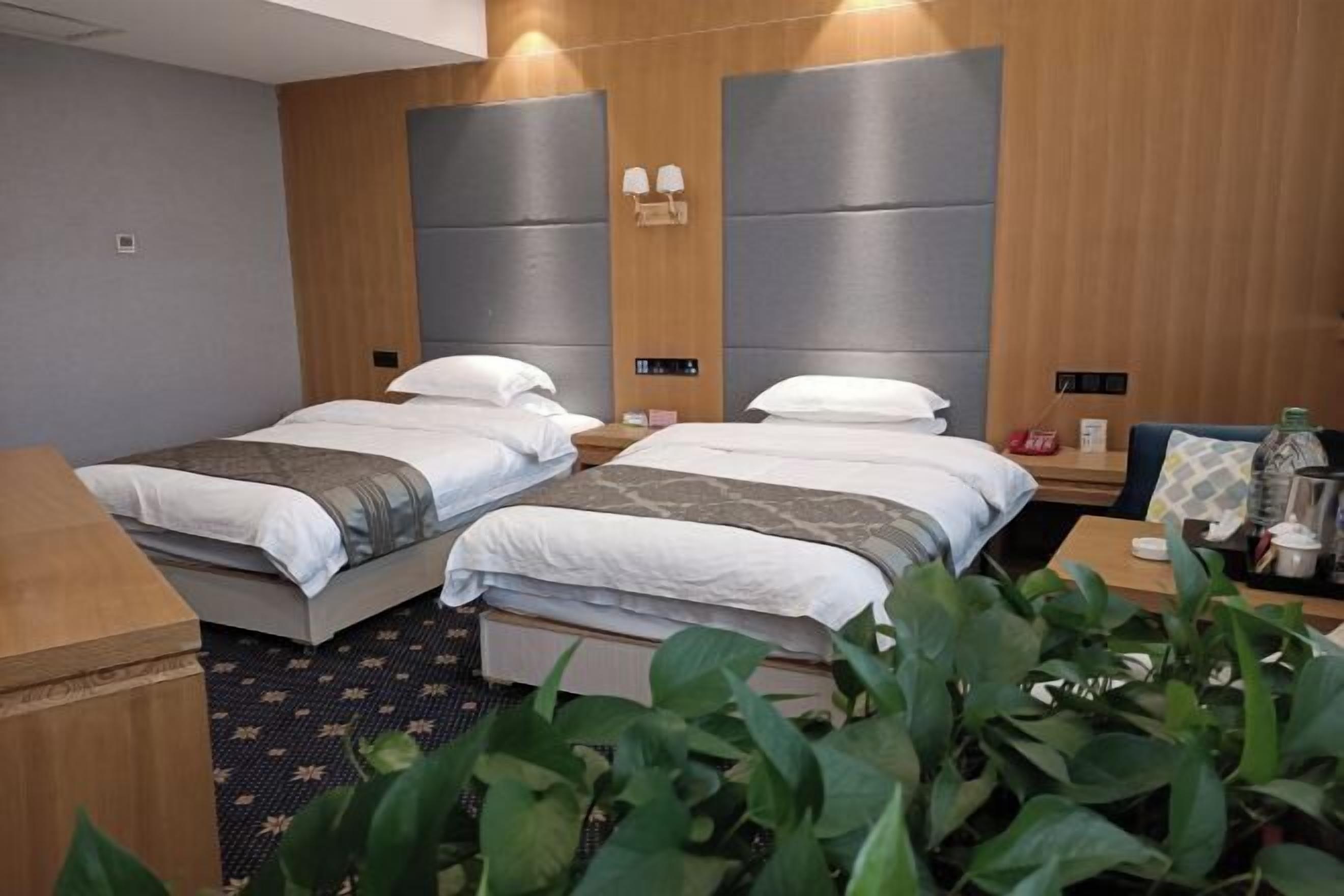 Habitación de hotel con dos camas, cabecero de madera, mesitas de noche y un escritorio pequeño con una silla.