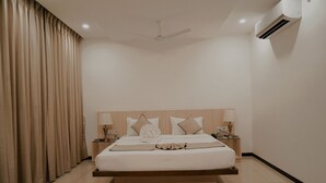 A bedroom with a bed, curtains, a ceiling fan, an air conditioner, and bedside lamps. - Pride Resort Ranakpur. (Desuri)