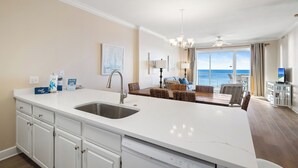 Een moderne keuken met een groot eiland, een eetgedeelte met rieten meubels en uitzicht op de oceaan.
