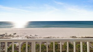 Uitzicht op een strand vanaf een balkon met een hekwerk, zandstrand en oceaan.