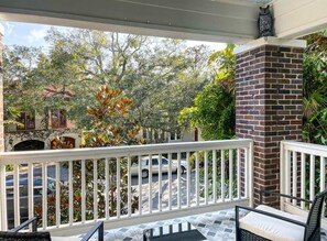 A balcony with a white railing, a brick column, and a view of a street with cars and trees.