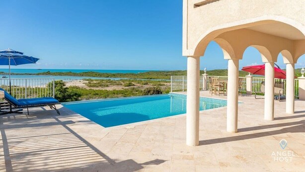 A pool area with a view of the sea, lounge chairs, and umbrellas. - Private Pool & Stunning Sunsets Near Chalk Sound (Providenciales)