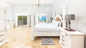 A spacious bedroom with a large bed, a nightstand, and a view of the ocean through a balcony. - Private Pool & Stunning Sunsets Near Chalk Sound (Providenciales)