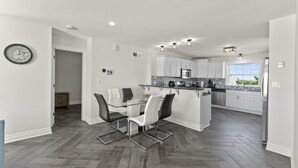 A modern kitchen with white cabinets, a central island, and a dining area with a glass table and chairs. - Cozy 3 Bedroom Lakefront Cottage (Blenheim)