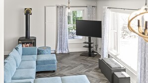 A modern living room with a sofa, ottoman, and a television. - Cozy 3 Bedroom Lakefront Cottage (Blenheim)