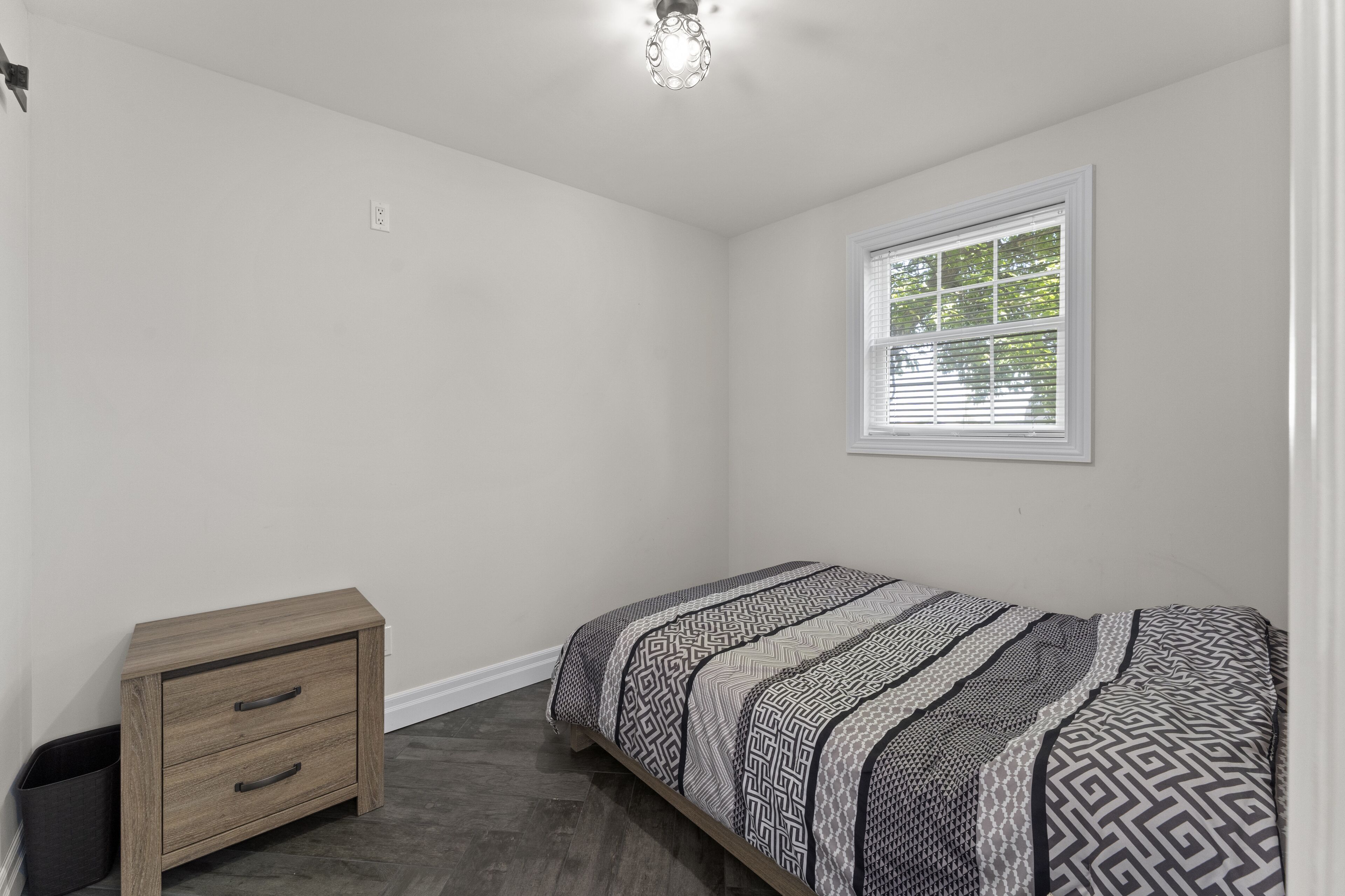 A bedroom with a bed, a nightstand, a window, and a ceiling light.