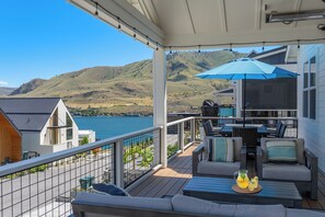 A deck with outdoor furniture, a grill, and a view of a lake and hills.