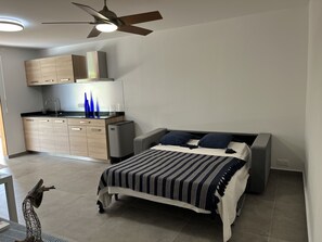 Enjoy a comfortable stay in this cozy room featuring a kitchenette with oven and microwave, a dining area with sink and countertop, and a bed with a striped bedspread.