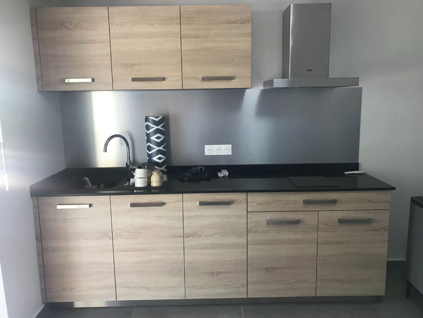 A modern kitchen with light wood cabinets, a black countertop, and stainless steel appliances.
