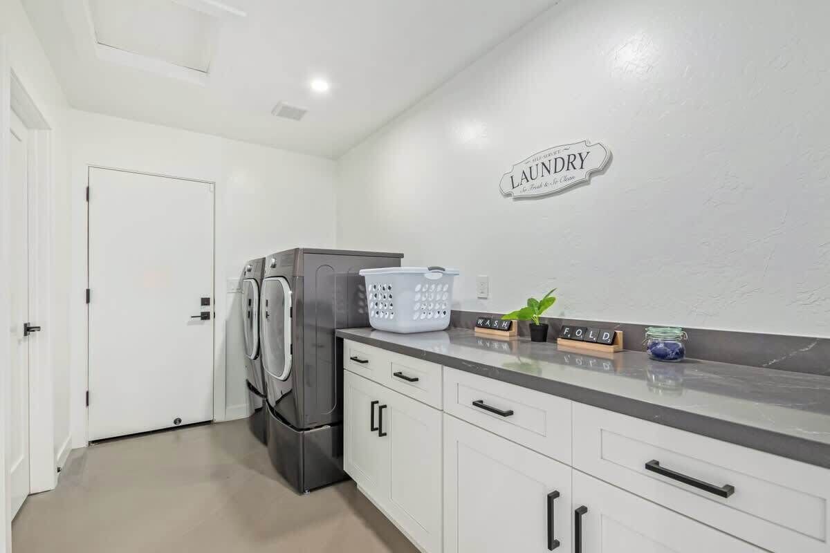 Zona de lavandería con lavadora, secadora, cesto de ropa y un letrero en la pared que dice 'LAUNDRY'.