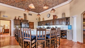 A spacious kitchen with a large island, wooden chairs, and hanging pendant lights.