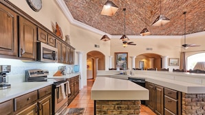 A spacious kitchen with a large island, wooden cabinets, and a brick ceiling.
