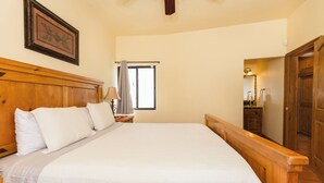A bedroom with a large bed, wooden headboard, a nightstand with a lamp, a framed picture on the wall, and a window with curtains.