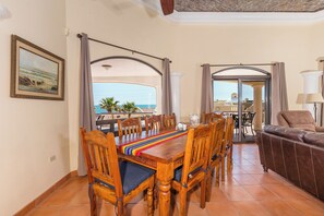 Zona pranzo con tavolo e sedie in legno, un runner colorato e vista sul mare attraverso porte vetrate.