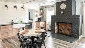 Une cuisine moderne avec une cheminée en briques, des armoires en bois et un coin repas comprenant une table ronde et des chaises.