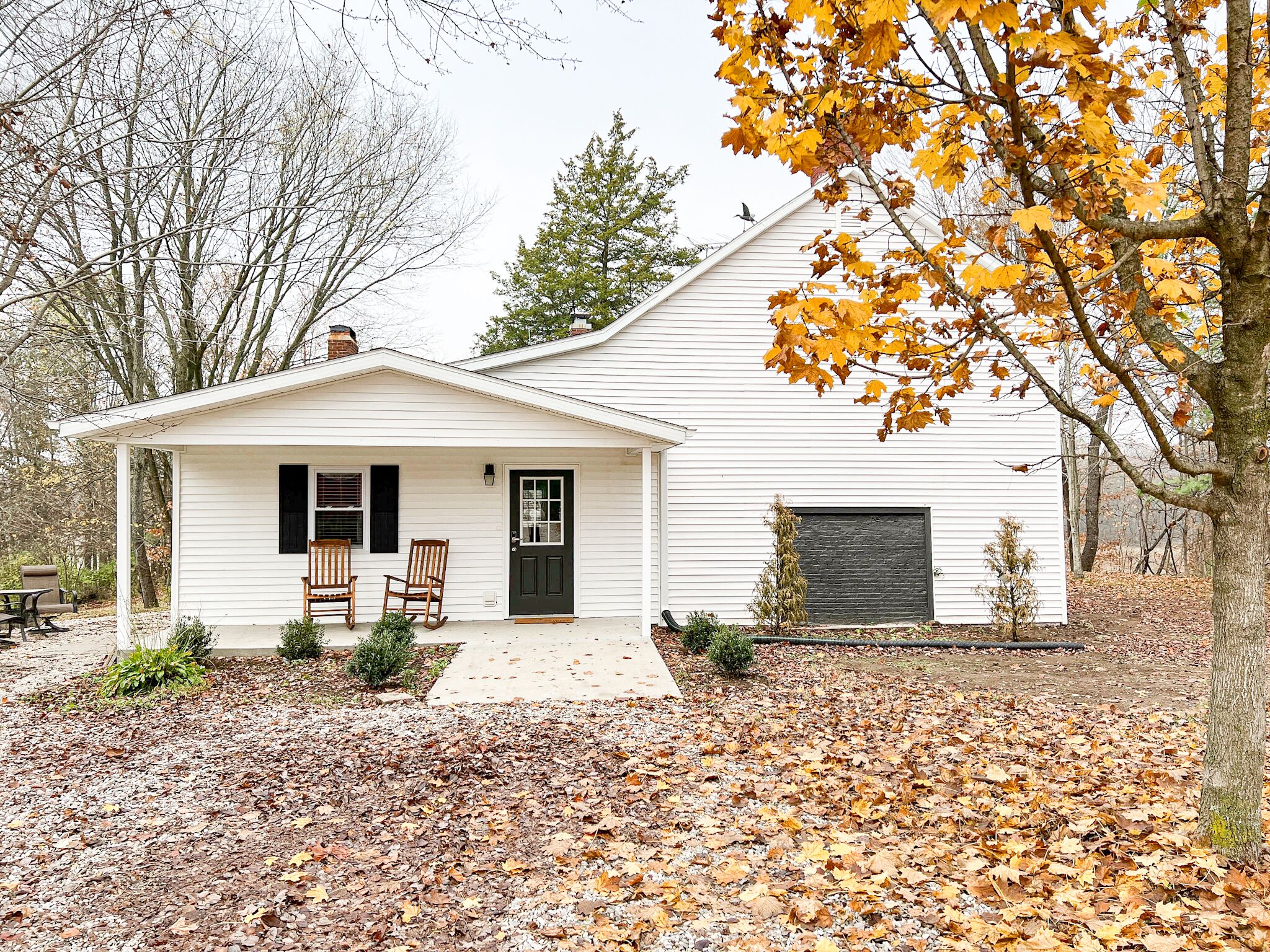 A white single-story house with a front porch, two rocking chairs, and a garage door.