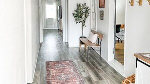 Un couloir doté d’un plancher en bois, d’un tapis à motifs, d’un banc, d’une plante en pot et d’un luminaire suspendu.