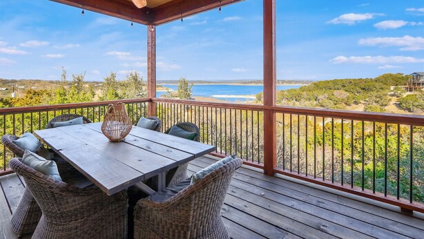 A wooden deck with a table and chairs, overlooking a beach and ocean.