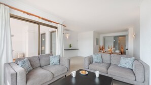 Una sala de estar moderna con dos sofás grises, una mesa de centro negra y una mesa de comedor con un plato de galletas.