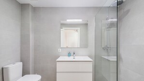 Un baño moderno con inodoro, lavamanos con espejo y ducha con mampara de vidrio.
