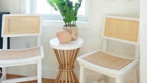 Una habitación con dos sillones blancos de mimbre, una pequeña mesa redonda con una planta en maceta y dos palas de madera en la pared.