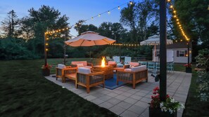 Une terrasse extérieure aménagée avec des meubles en osier, un foyer et des guirlandes lumineuses.