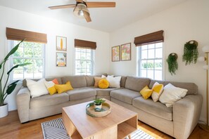Un salon moderne avec un canapé d’angle beige, une table basse en bois et une grande plante en pot.